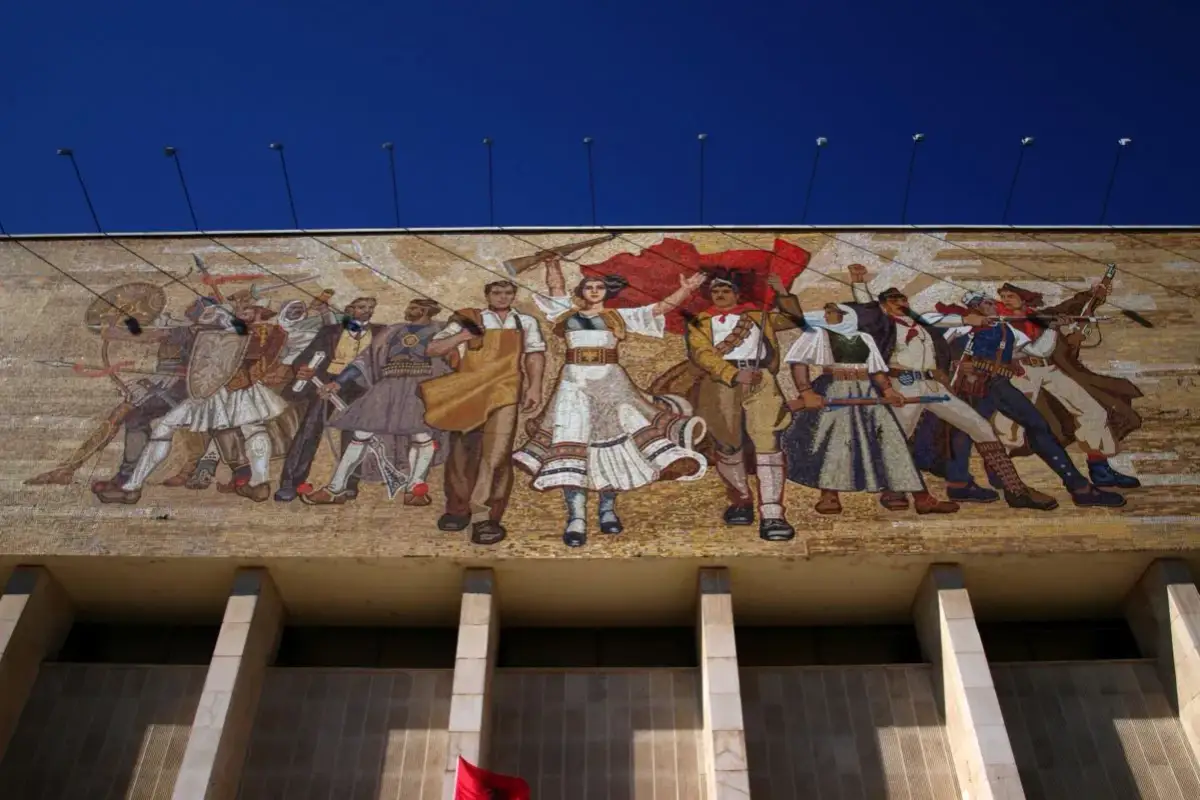 Mozaika w stylu socrealizmu przedstawia grupę ludzi w strojach ludowych, z bronią i flagami, symbolizujących walkę i jedność.