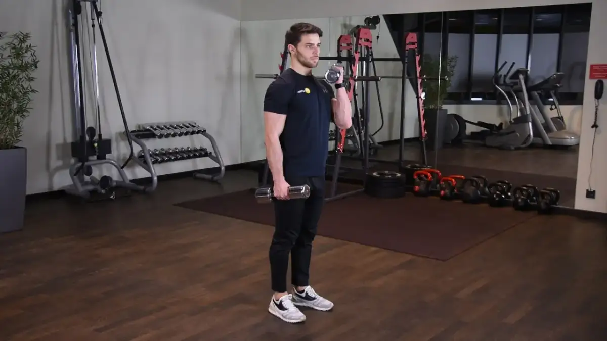 Mężczyzna wykonuje zottman curl z hantlem, ćwicząc biceps i przedramię. W tle siłownia z maszynami i ciężarami.