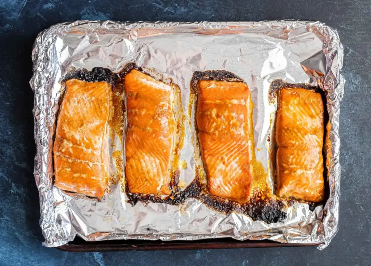 Cztery kawałki łososia na blasze wyłożonej folią aluminiową, gotowe do przygotowania sushi.