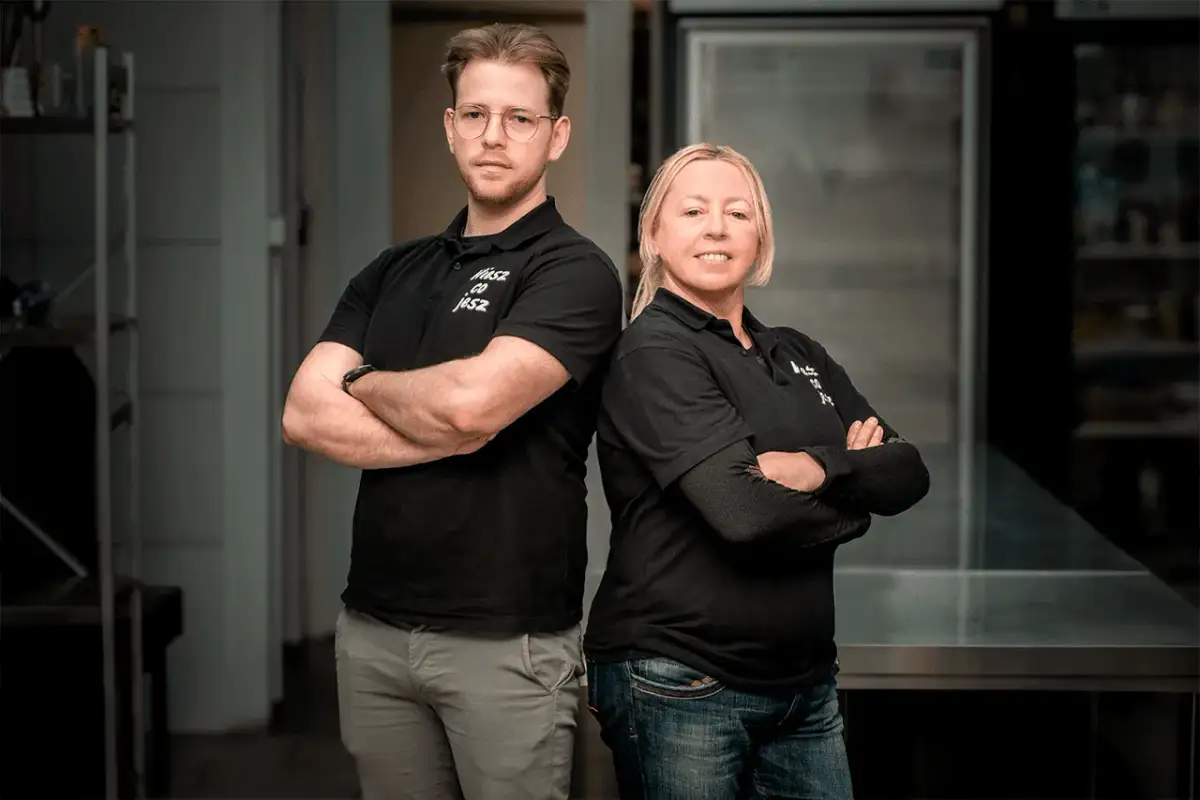 Para mężczyzny i kobiety w czarnych koszulkach z logo "Wiesz Co Jesz" stoją ze skrzyżowanymi rękami.