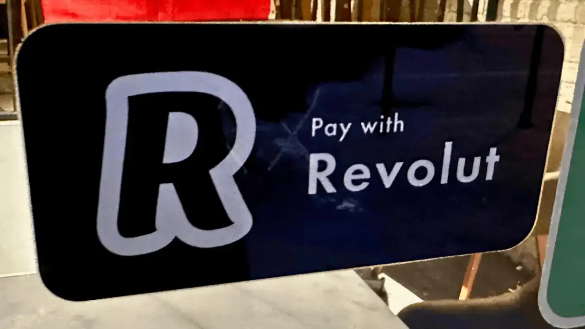 Znak informuje, jak płacić Revolutem. Widoczny duży symbol "R" i napis "Pay with Revolut".