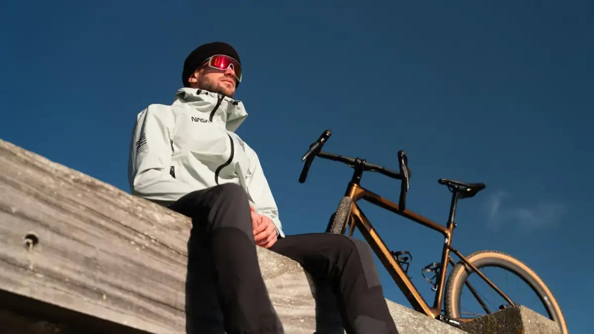 Mężczyzna w kurtce NASA i goglach patrzy w niebo obok swojego roweru. Idealny moment, by pomyśleć, jak przygotować rower do sezonu.