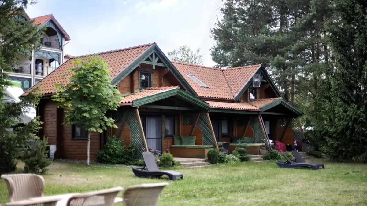Drewniany domek spa na Mazurach, otoczony zielenią. Leżaki zapraszają do relaksu.