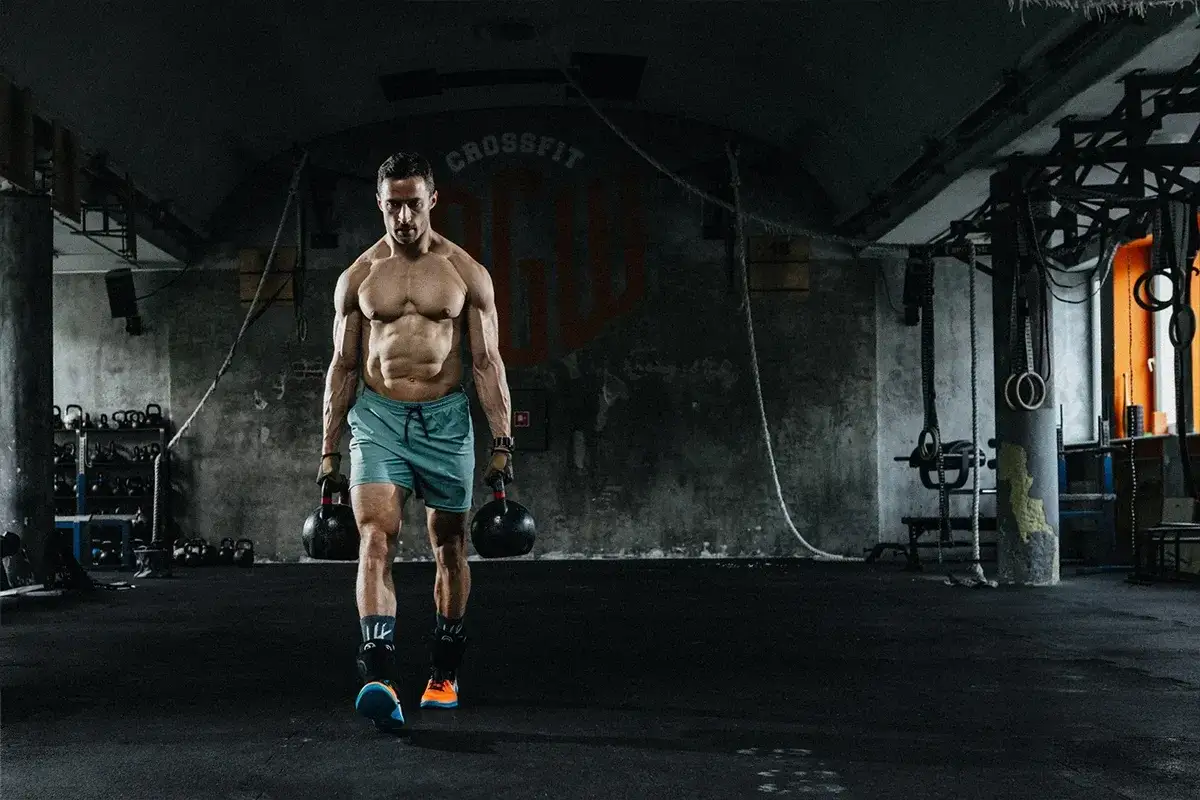 Mężczyzna z imponującą muskulaturą idzie z odważnikami w siłowni. To dowód, że crossfit dla kogo? Dla każdego, kto chce budować siłę i wytrzymałość!