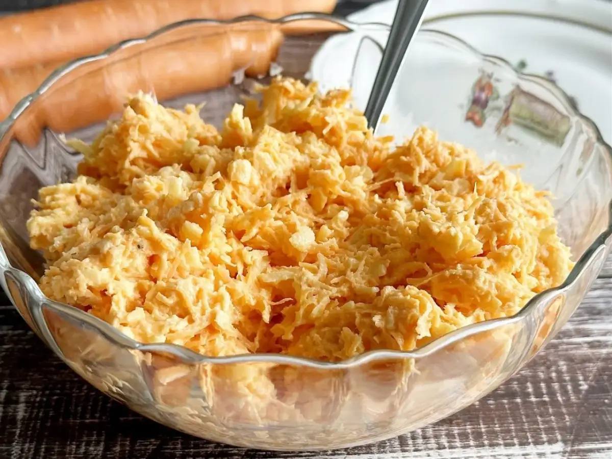 Pyszna surówka z marchewki w szklanej misie, gotowa do podania. Obok leżą świeże marchewki.