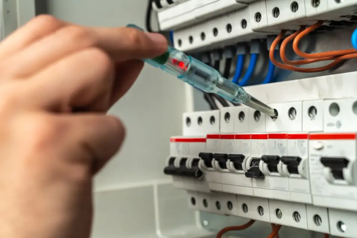 Dłoń z próbnikiem napięcia sprawdza zabezpieczenie skrzynki elektrycznej. Czerwona lampka próbnika świeci.