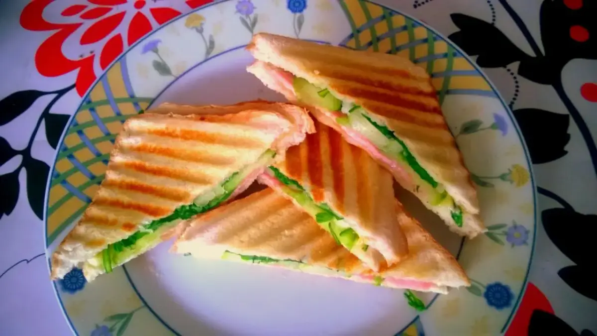 Chrupiące tosty z szynką, serem i świeżym ogórkiem na talerzu z kolorowym wzorem. Idealne na szybki lunch.