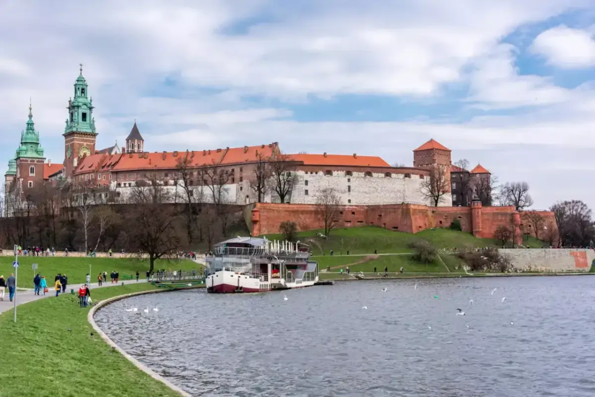 Zamek Królewski na Wawelu nad Wisłą, z łodzią i spacerującymi ludźmi.