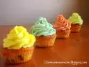 Cztery kolorowe muffiny z kremem: żółtym, miętowym, łososiowym i jasnozielonym.