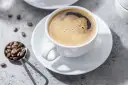 Aromatic coffee in a white cup, with beans on a spoon. Czy kawa jest lekkostrawna? To zależy od sposobu parzenia.