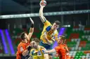 Gracz w żółtej koszulce rzuca piłkę do bramki, broniony przez zawodników w pomarańczowych strojach. Emocjonujący moment z meczu final four handball.