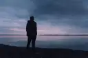 Samotny mężczyzna stoi nad jeziorem o zmierzchu, patrząc w dal. Czy to pesymista, kto to, zastanawia się nad mrocznym niebem i spokojną wodą?