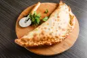 Złocisty calzone, czyli włoska pierożkowa pizza, leży na desce z krążkiem do pizzy i natką pietruszki.