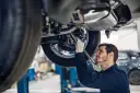 Mechanik w rękawiczkach naprawia podwozie auta. Zastanawiasz się, ile zarabia właściciel warsztatu samochodowego?