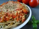 Talerz spaghetti z sosem pomidorowym i tofu, posypany serem i ziołami.