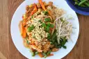 Pad Thai z kurczakiem, warzywami i orzeszkami ziemnymi na białym talerzu.