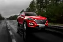 Czerwony Hyundai Tucson jedzie po mokrej drodze w deszczowy dzień. Warto pamiętać o filtrze CPL, którego zastosowanie poprawia widoczność w takich warunkach.