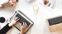 Kobieta pisze na laptopie, przygotowując wypowiedzenie umowy o dzieło. Obok świeca, muffinka i bukiet kwiatów.