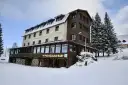 Hotel w Zieleńcu zimą, z widoczną wypożyczalnią nart i stosem drewna.