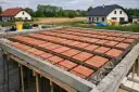 Budowa domu w toku. Widoczny strop gęstożebrowy z pustaków ceramicznych, przygotowany do zalania betonem.
