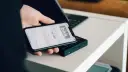 Dłoń trzyma smartfon z aplikacją Blik i kodem transakcji nad terminalem płatniczym.