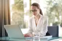 Kobieta w okularach pracuje na laptopie, szukając informacji, jak założyć działalność nierejestrowaną.