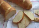 Chrupiąca bułka wrocławska, pokrojona w kromki, leży obok całej bagietki na lnianym obrusie.