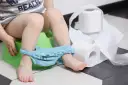Dziecko na nocniku, obok rolki papieru toaletowego. Wygląda na to, że ma wodnistą biegunkę.