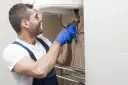 Instalator w niebieskich rękawiczkach dokręca zawór, pokazując, jak spuścić wodę z bojlera.
