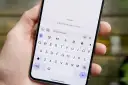 Dłoń trzyma smartfon z otwartą klawiaturą. Widoczny komunikat "RCS chat with Judy" sugeruje, jak włączyć czat RCS.
