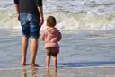 Ojciec i dziecko na plaży, cieszący się wspólnym urlopem ojcowskim 9 tygodni.
