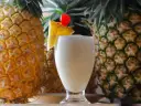 Pina Colada na mleczku kokosowym czy na śmietance? Orzeźwiający drink z ananasem i wisienką, otoczony dojrzałymi owocami.