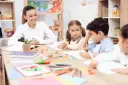 Uśmiechnięta nauczycielka przygląda się dzieciom podczas lekcji. To idealne miejsce na podanie o pracę nauczyciel.