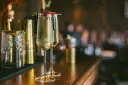 Dwa kieliszki musującego drinku z Prosecco i Cava, ozdobione malinami, stoją na barze obok stylowych akcesoriów.