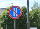 Znak B37 zakazujący postoju. Dwa pionowe białe paski na niebieskim tle, przekreślone czerwoną linią.