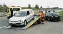 Holowanie uszkodzonego samochodu na lawetę, obok stoi policja i drugi samochód.