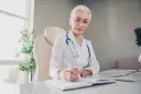 Lekarka w białym kitlu z niebieskim stetoskopem pisze w notatniku. Pytanie o wypalenie zawodowe L4 kto wystawia, może być skierowane do niej.