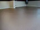 Nowoczesna posadzka z pianobetonu w neutralnym kolorze, otoczona jasnymi płytkami ściennymi i niebieską listwą przypodłogową.