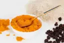 Miseczka pełna intensywnej przyprawy curry, obok ryż i rodzynki. Złota łyżeczka zanurzona w aromatycznym proszku.