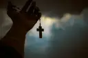 Dłoń trzyma paciorki różańca z krzyżem, symbolizując poszukiwanie prawdy w obliczu niepewności, jak agnostycyzm.