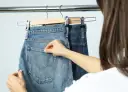 Dwie pary jeansów wiszą na wieszakach. Kobieta pokazuje, jak wieszać spodnie na wieszaku, chwytając za kieszeń.