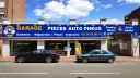 Garage avec enseigne bleue et jaune, deux voitures garées devant, sous un ciel bleu avec des nuages.