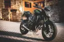Czarny motocykl Kawasaki na brukowanej ulicy, z budynkami w tle.