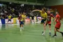 Gracz w żółtej koszulce rzuca piłkę ręczną podczas meczu. W tle kibice i zawodnicy w czerwonych strojach. Stal Gorzów walczy o zwycięstwo.