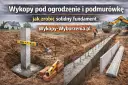 Solidny fundament pod ogrodzenie w trakcie budowy. Betonowy słup z poziomicą, łopata i koparka w tle.