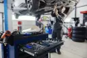 Warsztat samochodowy: mechanik pracuje pod podniesionym autem, wózek z narzędziami na pierwszym planie.
