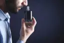 Mężczyzna wącha perfumy z buteleczki.