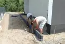 Dwóch mężczyzn pracuje nad przygotowaniem podłoża pod kostkę, układając obrzeża.