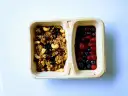 Dwie przegródki pojemnika: jedna z granolą z orzechami i suszonymi owocami, druga z jagodami i truskawkami. Czy kasza jaglana ma gluten? Ta granola wygląda na bezglutenową!