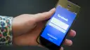 Eine Hand hält ein Smartphone mit der Facebook-Anmeldeseite.
